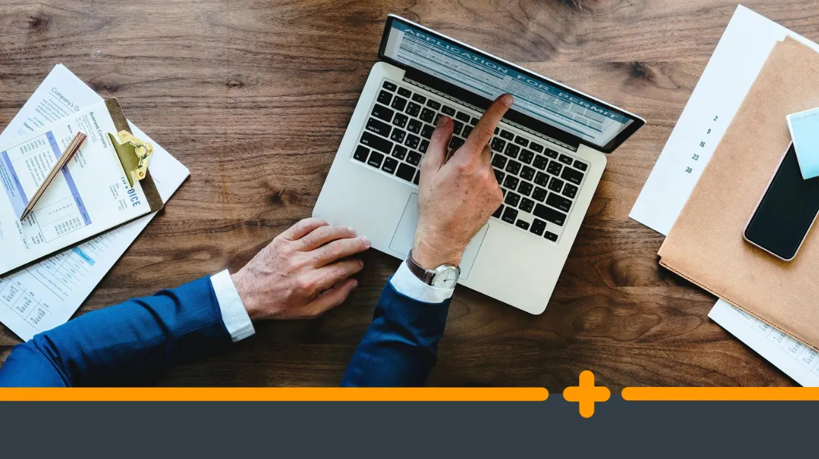 Ręce mężczyzny w garniturze pracującego na laptopie przy biurku z dokumentami i telefonem