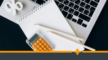 Notatnik w kratkę, kalkulator i ołówki leżące na klawiaturze laptopa — symbol planowania finansów lub obliczania kosztów pożyczki.